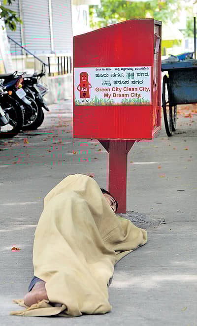 ಅಂಚೆಪೆಟ್ಟಿಗೆಯ ಬುಡದಲ್ಲಿ ಮಲಗಿ ನಿದ್ರಿಸುತ್ತಿರುವ ಈ ವ್ಯಕ್ತಿ ಜಾಹೀರಾತಿನಲ್ಲಿ ಬರೆದಿರುವಂತೆ ಹಸಿರು ನಗರ ಹಾಗೂ ಸ್ವಚ್ಛ ನಗರದ ಕನಸು ಕಾಣುತ್ತಿರಬಹುದೇ? ಚಾಮರಾಜಪೇಟೆಯಲ್ಲಿ ಭಾನುವಾರ ಕಂಡುಬಂದ ದೃಶ್ಯ.   -ಪ್ರಜಾವಾಣಿ ಚಿತ್ರ