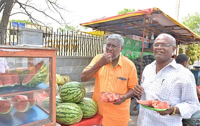 ಕೋಲಾರದ ಟಿ.ಚನ್ನಯ್ಯ ರಂಗಮಂದಿರ ಮುಂಭಾಗದ ಅಂಗಡಿಯಲ್ಲಿ ಕಲ್ಲಂಗಡಿ ಹಣ್ಣು ತಿನ್ನುತ್ತಿರುವ ಸಾರ್ವಜನಿಕರು