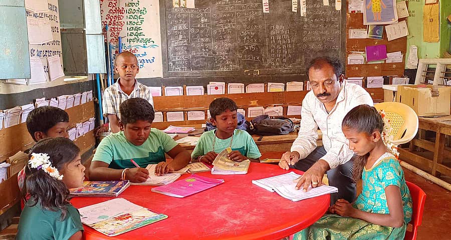 ವಿಜಯಪುರ ಹೋಬಳಿ ಗೊಡ್ಲುಮುದ್ದೇನಹಳ್ಳಿ ಗ್ರಾಮ ಪಂಚಾಯಿತಿ ವ್ಯಾಪ್ತಿಯ ಚಿನುವಂಡನಹಳ್ಳಿ ಸರ್ಕಾರಿ ಶಾಲೆಯಲ್ಲಿ ಮಕ್ಕಳಿಗೆ ಪಾಠ ಹೇಳಿಕೊಡುತ್ತಿದ್ದ ಶಿಕ್ಷಕ.