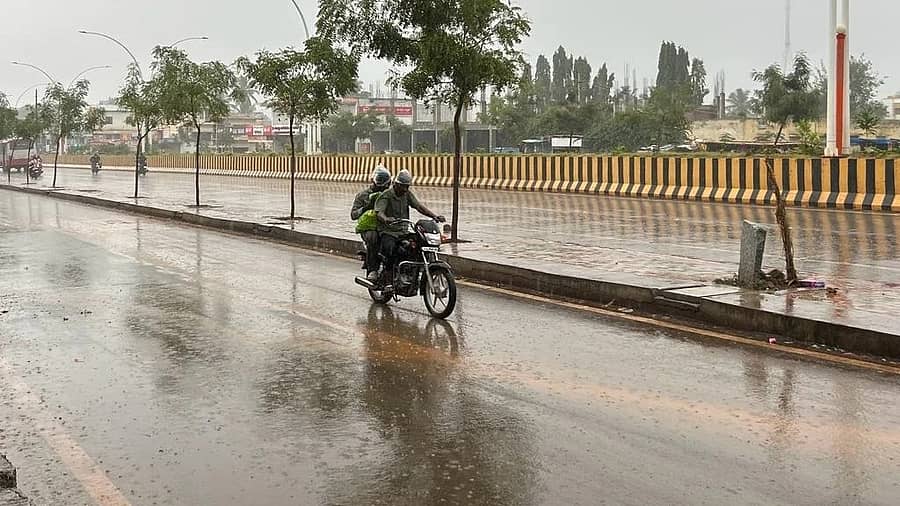 Two people rise a two-wheeler in the rain on BD Road in Chitradurga on Saturday. DH Photo