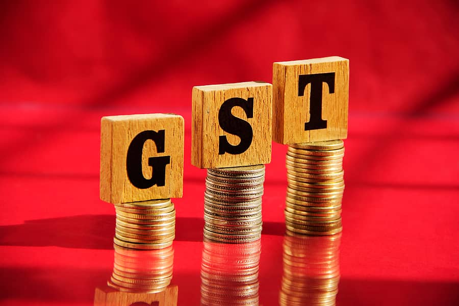 Wooden letters GST and money coin stack on red table background, financial concept