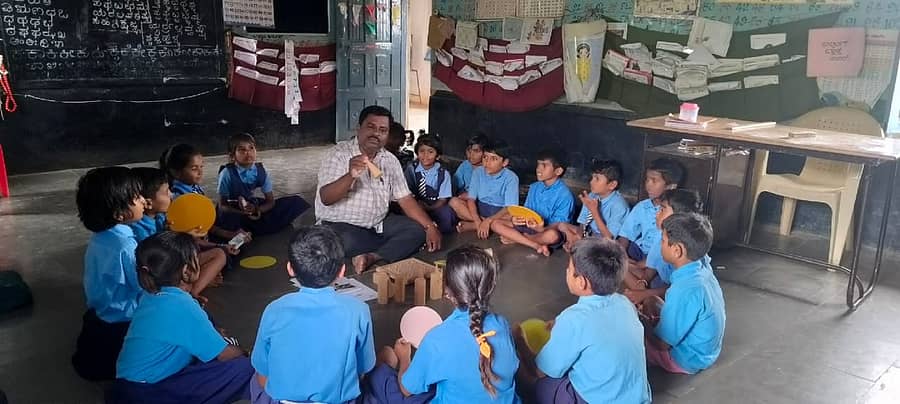 ಮಕ್ಕಳ ಜತೆಗೆ ತರಗತಿ ಕೊಠಡಿಯಲ್ಲಿ ಕುಳಿತು ಮಕ್ಕಳಿಗೆ ಚಟುವಟಿಕೆ ಆಧಾರದಲ್ಲಿ ಕಲಿಸುತ್ತಿರುವ ಶಿಕ್ಷಕ ಸಂಗಪ್ಪ ಯಾಳವಾರ