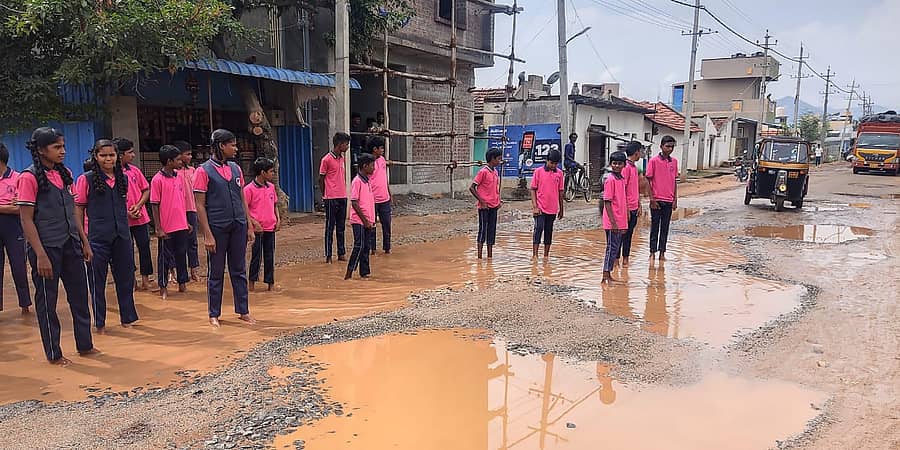 ಹನೂರು ಪಟ್ಟಣದಿಂದ ಲೊಕ್ಕನಹಳ್ಳಿಗೆ ಸಂಪರ್ಕ ಕಲ್ಪಿಸುವ ರಾಜ್ಯ ಹೆದ್ದಾರಿ ಗುಂಡಿಗಳಲ್ಲಿ ಗೌತಮ್ ಶಾಲೆ ವಿದ್ಯಾರ್ಥಿಗಳು ನಿಂತಿರುವುದು