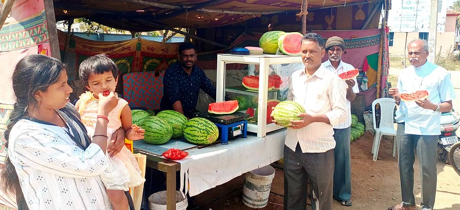 ಮಧುಗಿರಿ ತಾಲ್ಲೂಕು ಕಚೇರಿ ಮುಂಭಾಗವಿರುವ ಹಣ್ಣಿನ ಅಂಗಡಿ ಮುಂದೆ ಕಲ್ಲಂಗಡಿ ತಿನ್ನುತ್ತಿರುವ ಜನ
