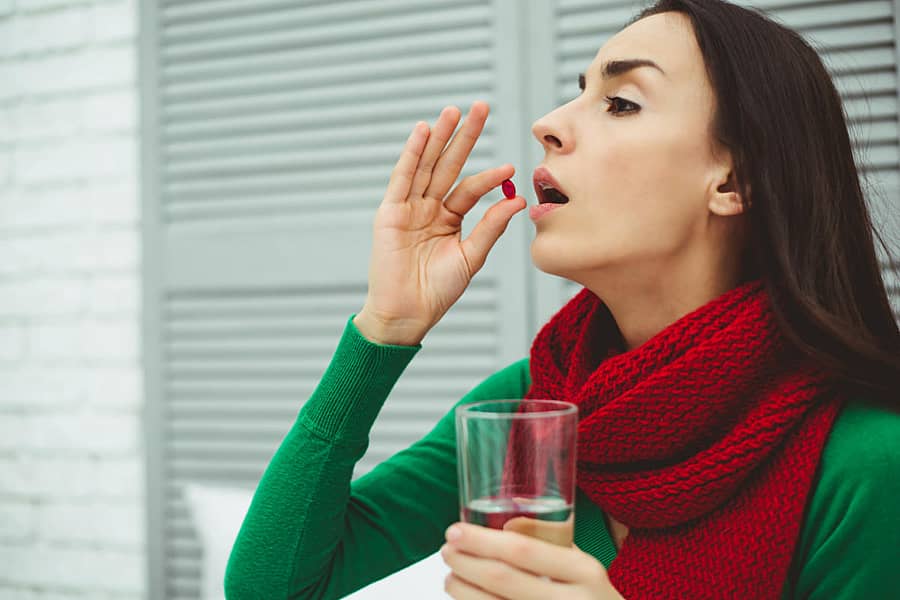 Reception of medicines. Photo of a young woman in a red scarf on the bed at home that keeps the tablet in his hand and glass of water. The concept of health and disease.