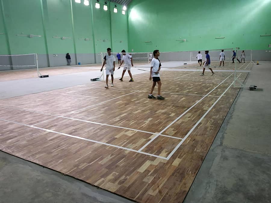 ಹೊಸದಾಗಿ ನೆಲಹಾಸು ಹಾಕಿರುವ ಒಳಾಂಗಣ ಕ್ರೀಡಾಂಗಣದಲ್ಲಿ ಮಕ್ಕಳು ಬ್ಯಾಡ್ಮಿಂಟನ್ ಆಡುತ್ತಿರುವುದು