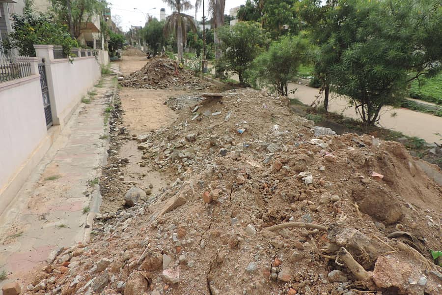 ಮಳೆ ನೀರು ನಿಲ್ಲದಂತೆ ತಡೆಯಲು ರಸ್ತೆಯಲ್ಲೇ ಕಸ ಮಿಶ್ರಿತ ಮಣ್ಣನ್ನು ಗುಡ್ಡೆ ಹಾಕಿರುವುದು