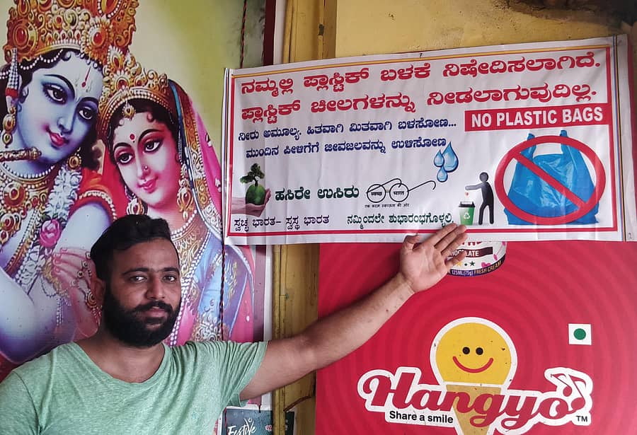 ಅಂಗಡಿಯೆದುರು ಹಾಕಿರುವ ಫಲಕ ತೋರಿಸುತ್ತಿರುವ ಹರೀಶ ಮೋದಿ