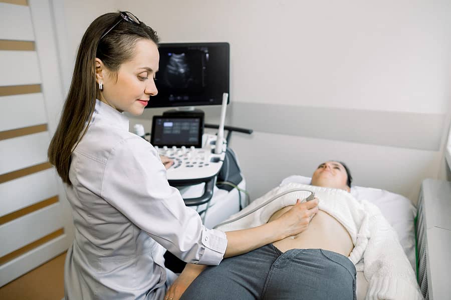 Young Caucasian pregnant woman undergoing abdominal ultrasound scan in clinic.Young Caucasian pregnant woman undergoing abdominal ultrasound scan in clinic