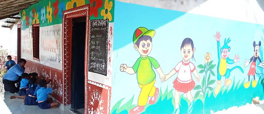 ಶಾಲೆಯ ಗೋಡೆಯ ಮೇಲೆ ಬಿಡಿಸಿರುವ ವರ್ಲಿ ಕಲೆಯನ್ನು ಕಲಿಯುತ್ತಿರುವ ಮಕ್ಕಳು