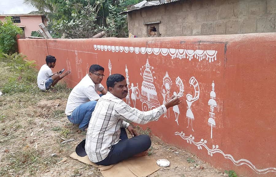 ಶಾಲೆಯ ಕಾಂಪೌಂಡ್ ಗೋಡೆ ಮೇಲೆ ಚಿತ್ರಿಸುತ್ತಿರುವ ಶಿಕ್ಷಕ ಬಿ.ಆಂಜನೇಯ ಮತ್ತು ಶಿವಕುಮಾರ.