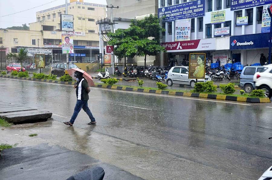 ಹಾಸನದ ಬಿ.ಎಂ ರಸ್ತೆಯಲ್ಲಿ ವ್ಯಕ್ತಿಯೊಬ್ಬರು ಕೊಡೆ ಹಿಡಿದು ಸಾಗುತ್ತಿರುವ ದೃಶ್ಯ.