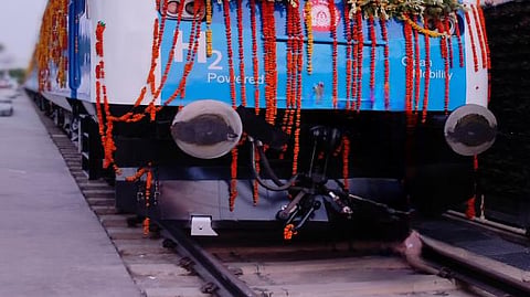 Front view of a blue and white hydrogen-powered train decorated with floral garlands.