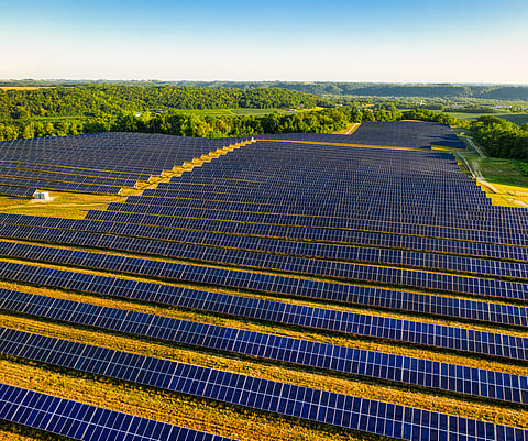 Aerial view of rows of solar photovoltaic panels covering a large green landscape.