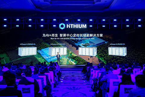 HiTHIUM executive presenting 8-hour-native energy storage systems on stage, with battery containers and an AI data center illustration displayed on the screen behind him.