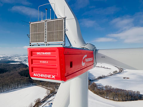 Close-up view of a Nordex Delta4000 N149/5.X wind turbine with its red nacelle and rotor extending over a snow-covered German landscape.