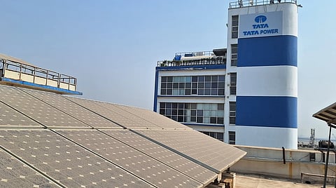 Tata Power solar photovoltaic panels installed across a rooftop, with a Tata Power building and branded tower visible in the background.