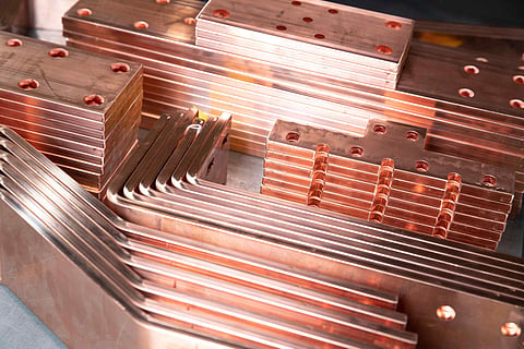 Stacked copper busbars and flat copper bars with drilled holes and polished surfaces, illustrating copper components used in electrical systems.