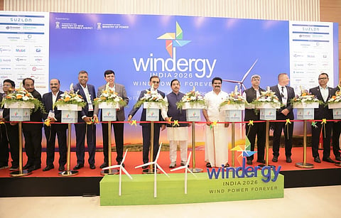Union Minister Shri Pralhad Joshi and other dignitaries stand behind a ceremonial ribbon with flower arrangements at the Windergy India 2026 inauguration, against a blue event backdrop featuring wind energy branding.