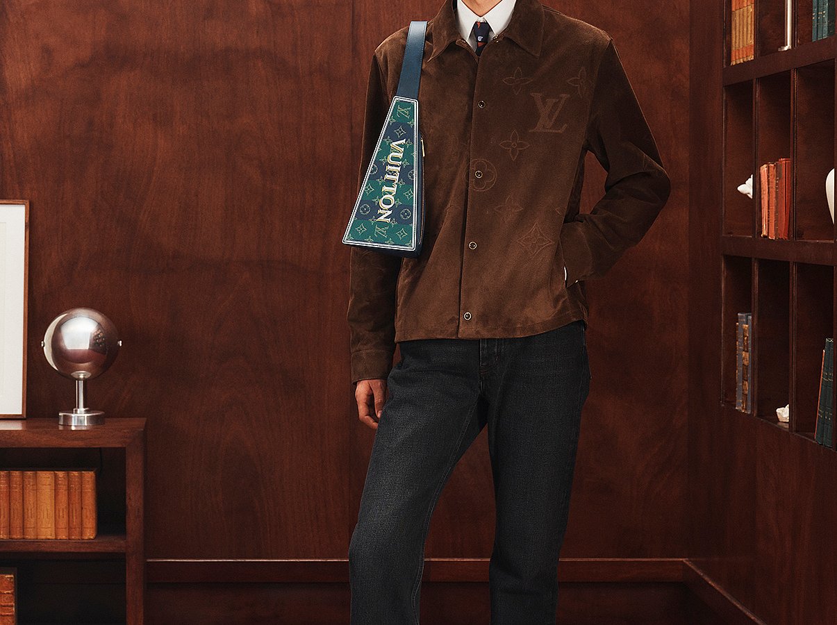 Model wearing a navy Louis Vuitton men’s cap with a brown suede jacket and dark denim.