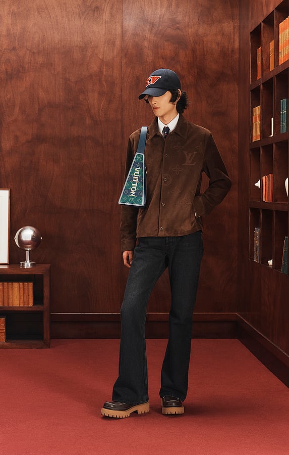 Model wearing a navy Louis Vuitton men’s cap with a brown suede jacket and dark denim.