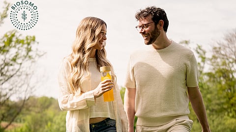 Man and woman walking in tall grass with Biosomo supplement bottle