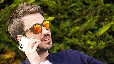 Man wearing reflective sunglasses and talking on a smartphone outdoors