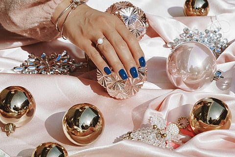 Hand with pearl ring and blue nails resting on holiday ornaments