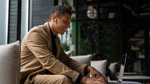 Man in tan suit using laptop with earbuds indoors