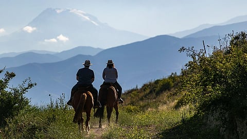 Two travelers horseback riding in Mendoza with Andes mountains behind