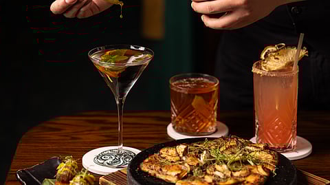 Bartender adds drops to martini beside colorful cocktails and Nikkei dishes