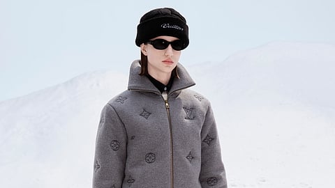 Model in gray Monogram jacket and navy pants holding blue LV duffel bag