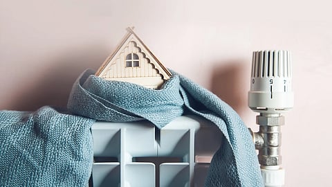 Small wooden house wrapped in a blue scarf on top of a radiator