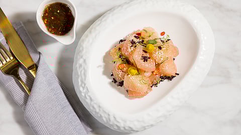 Pomelo salad with chili and herbs served in white bowl beside gold cutlery