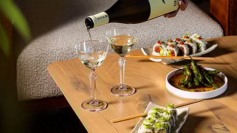 Sushi plates and sake being poured on a wooden table