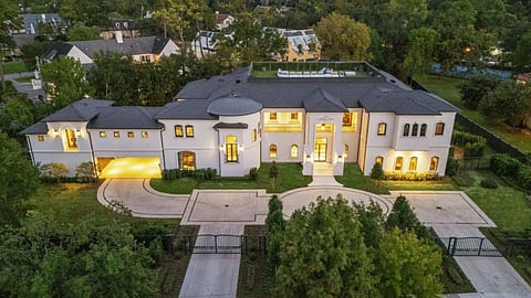 Aerial view of a grand Memorial-area estate with gated entry, circular drive, and rooftop terrace