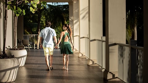 Couple walking hand in hand along a sunlit outdoor corridor at Bahia Beach