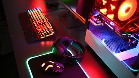 RGB-lit gaming desk with headset, keyboard, mouse, and a desktop PC glowing in red and green lights
