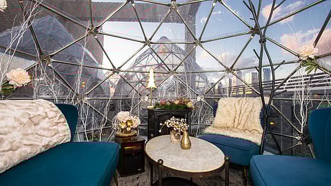 Interior of a teardrop rooftop igloo with plush seating, décor, and city views
