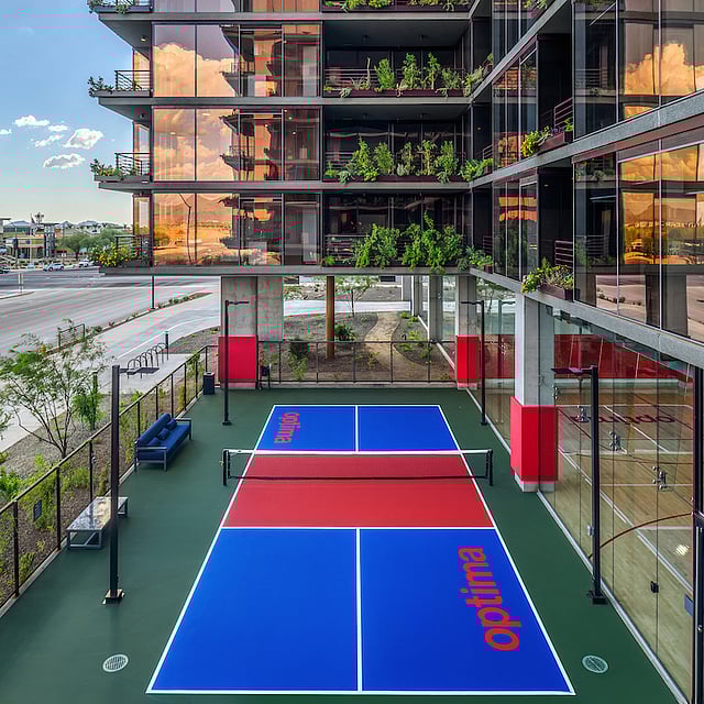 Outdoor pickleball court surrounded by glass walls and planted balconies at Optima McDowell Mountain