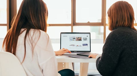 Two people seated at a table reviewing a website on a laptop