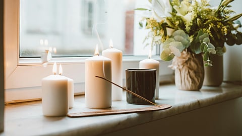 Lit white candles and incense on a windowsill beside fresh flowers, creating a calm atmosphere