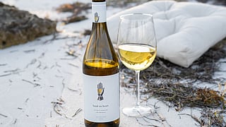 Hand on Heart non-alcoholic wine bottle and glass resting on sand