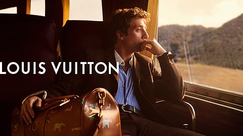Jeremy Allen White sits on a train with a Louis Vuitton keepall, gazing at the passing landscape