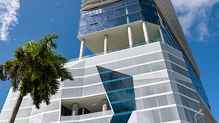 Modern high-rise hotel in downtown Miami with glass facade and palm trees below