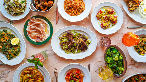 Overhead view of an Italian lunch spread with pasta, seafood, meats, vegetables, and cocktails
