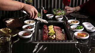 Premium beef grilling tableside at Jeong Yuk Jeom, surrounded by small Korean dishes and cocktails