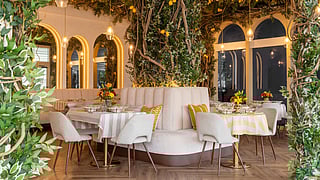 Interior of Nouveau Miami restaurant with greenery-covered walls, arched mirrors, and dining tables