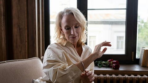 Woman seated by a window adjusting a delicate bracelet in a softly lit living room