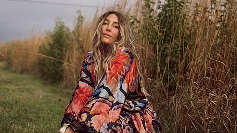 Caitlyn Warakomski crouching in a floral look in tall grass by the water